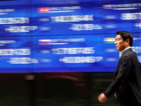 ک رهگذر در حال عبور از کنار مانیتور برقی است که شاخص قیمت سهام کشورهای مختلف را در خارج از بانکی در توکیو، ژاپن، در ۲۲ مارس ۲۰۲۳ نشان می‌دهد