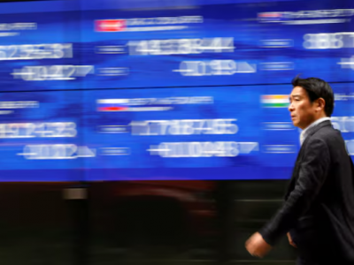 ک رهگذر در حال عبور از کنار مانیتور برقی است که شاخص قیمت سهام کشورهای مختلف را در خارج از بانکی در توکیو، ژاپن، در ۲۲ مارس ۲۰۲۳ نشان می‌دهد